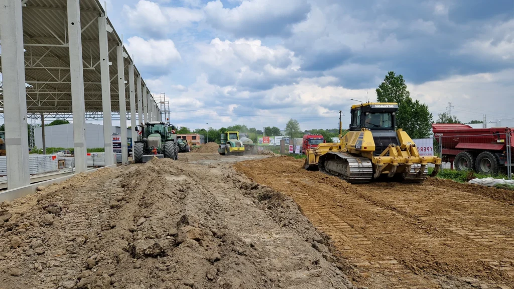 żółta koparka stabilizująca grunt podczas prac budowlanych obok niej trzy inne maszyny budowlane koloru żółtego